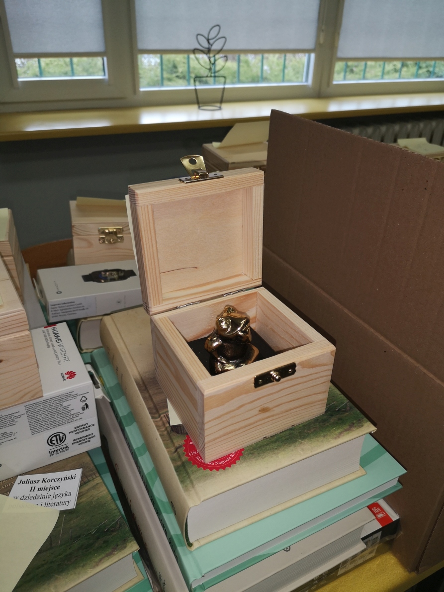 Statuetka złotej żaby w drewnianym pudełku oraz książki i watchhat huawei
