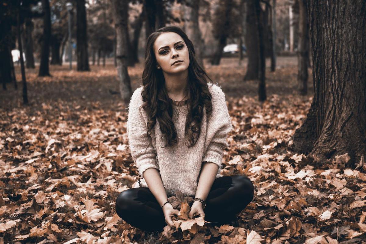 Kobieta siedzi w jesiennych liściach między drzewami