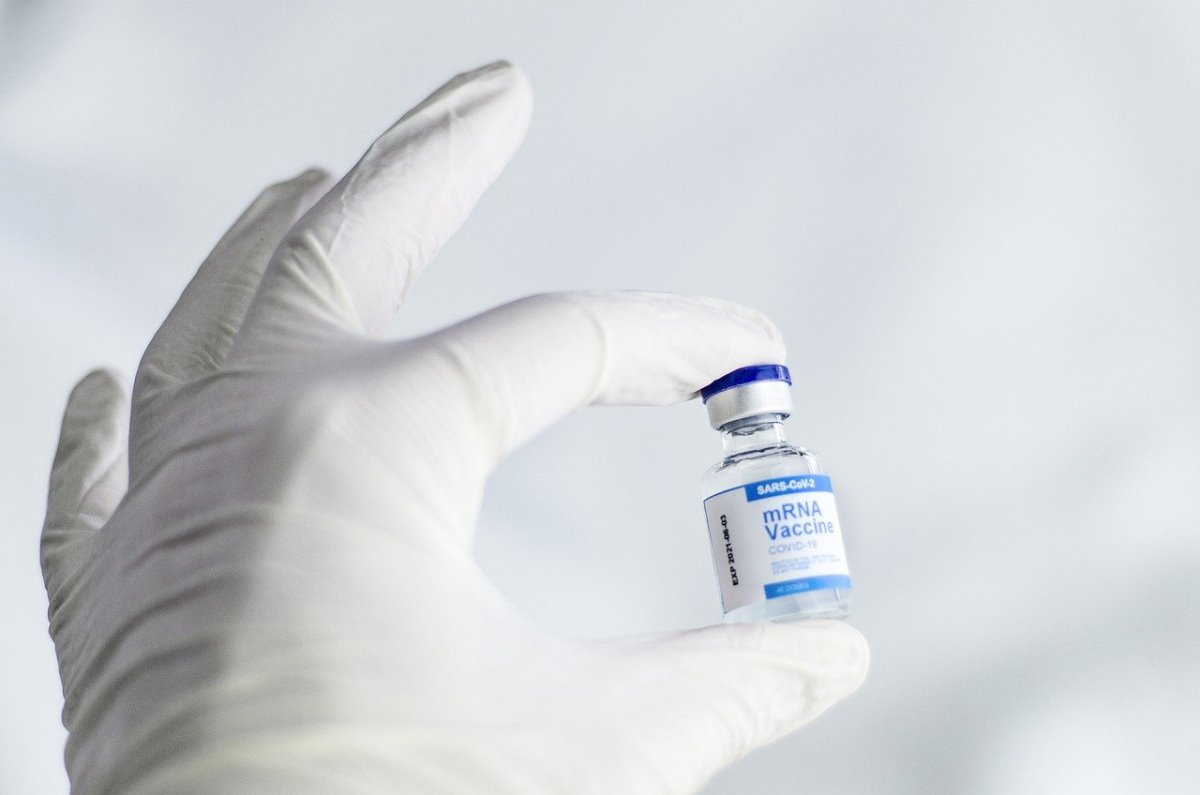 Szczepionka na CoviD trzymana w palcach dłoni w rękawiczce chirurgicznej