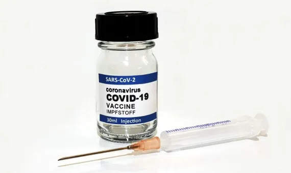 Fiolka ze szczepionką, przed nią leży pusta strzykawka