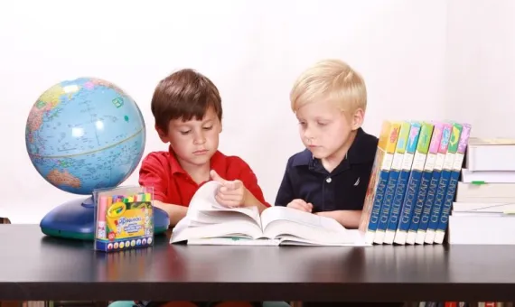 Dzieci czytają książkę przy stole, na stole książki i globus