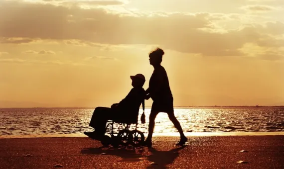 Kobieta prowadząca osobę z niepełnosprawnością ruchową na wózku po plaży