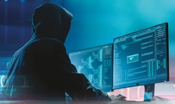 Osoba w kapturze przed monitorami komputerowymi