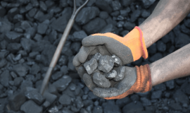 Węgiel trzymany w dłoniach przy hałdzie węgla z łopatą